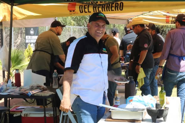 Parrillero sonriendo junto a su mesa de trabajo bajo una carpa