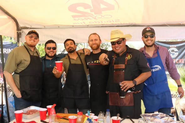 Equipo parrillero con mandiles posando bajo su carpa