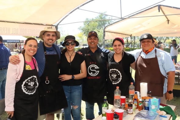 Equipo de damas y caballeros parrilleros con mandiles frente a su mesa